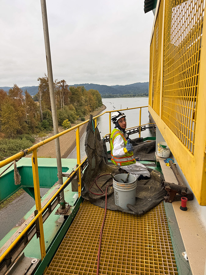 Long Painting crew member working on an elevated platform above a waterway