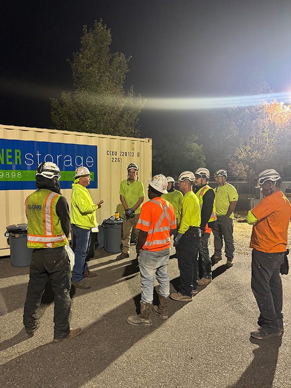 Long Painting crew gathered for a pre-shift safety briefing in the field at night